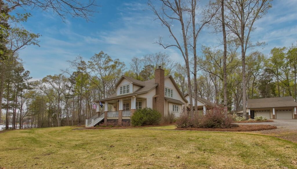 Two-story brick and white colonial home with garage on wooded property in early spring.