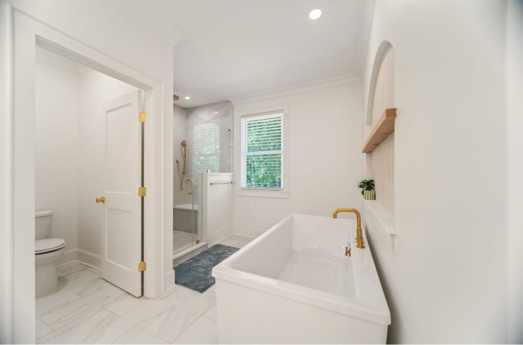 Modern bathroom with freestanding white soaking tub, separate shower enclosure, toilet, and brass fixtures