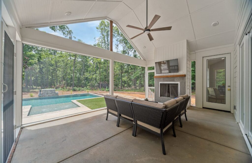 Screened porch with ceiling fan overlooking swimming pool and fireplace in wooded backyard