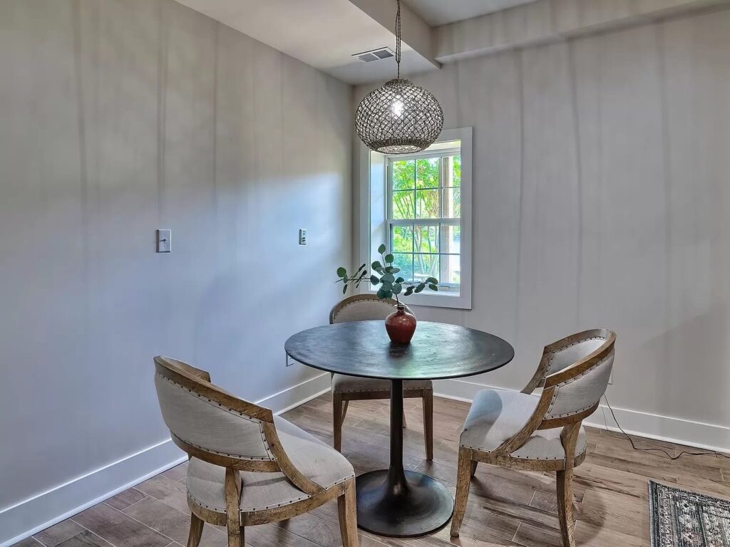 Modern dining room with round table, upholstered chairs, pendant light, and garden window with natural light.