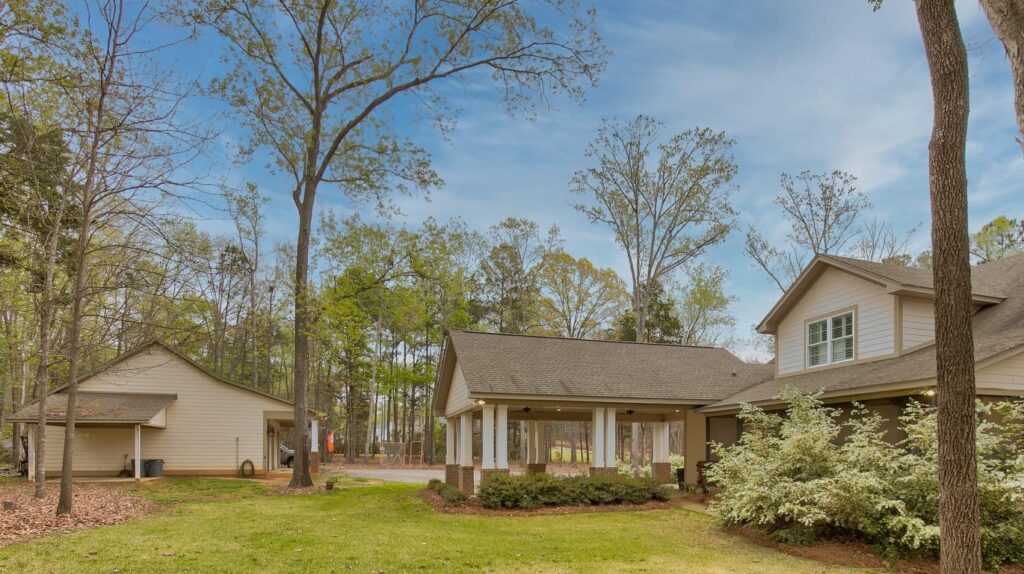 Spacious two-story home with wraparound porch surrounded by tall pine trees and manicured lawn.