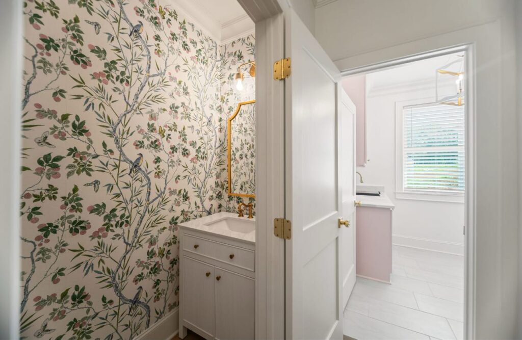 Modern bathroom with floral wallpaper, white vanity, gold fixtures, and glass shower enclosure