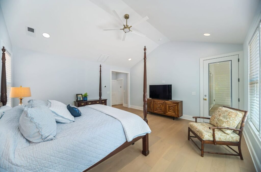 Spacious master bedroom with four-poster bed, wooden TV stand, sitting chair, and vaulted ceiling with ceiling fan.