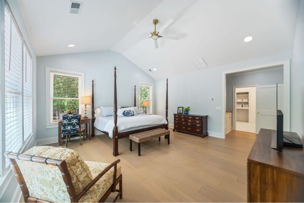 Spacious master bedroom with four-poster bed, light blue walls, wooden floors, and large windows.