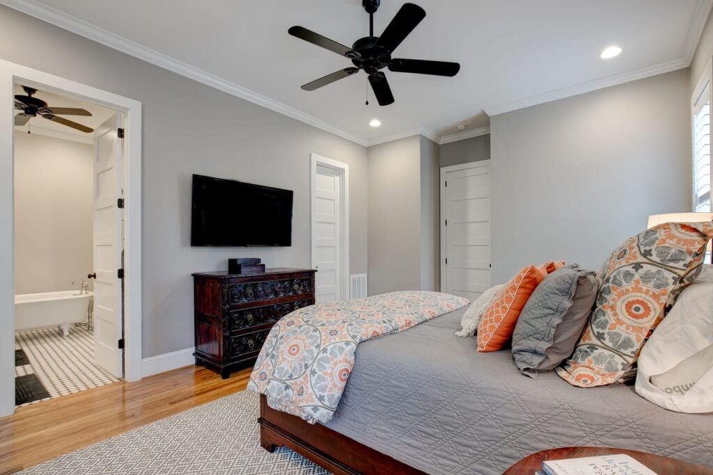 Master bedroom with king bed, dark wood dresser, wall-mounted TV, ceiling fan, and ensuite bathroom entrance.