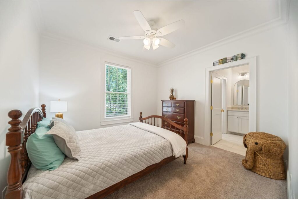 Bright bedroom with wooden bed, dresser, ceiling fan, window with green shutters, and wicker storage basket.