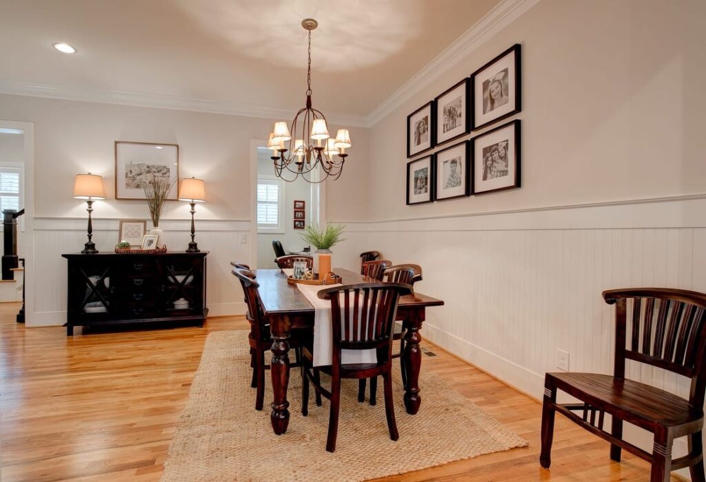 Elegant dining room with dark wood table, chairs, and buffet, pink walls with white wainscoting, and framed artwork.