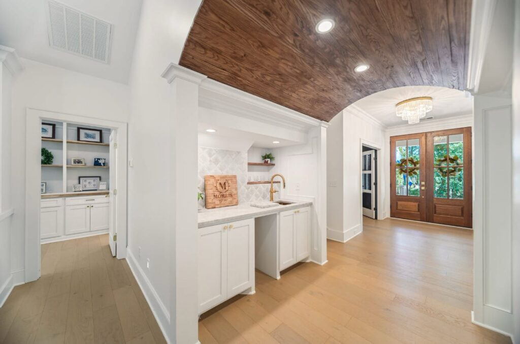 Modern kitchen with white cabinetry, wood ceiling, and open floor plan leading to entryway with glass doors.