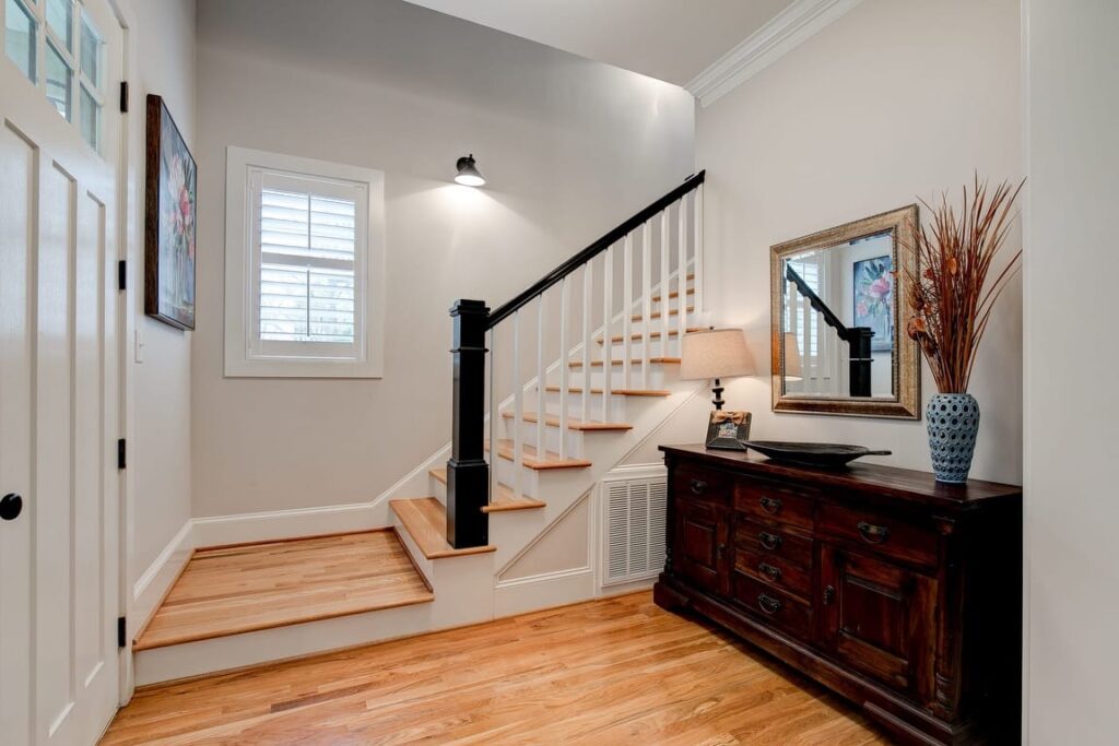 Modern foyer with wooden staircase, black railings, hardwood floors, dark wood dresser, and decorative mirror.