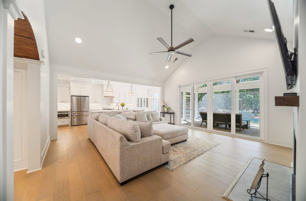 Modern open-concept living room with beige sectional sofa, ceiling fan, and sliding glass doors overlooking outdoor space.