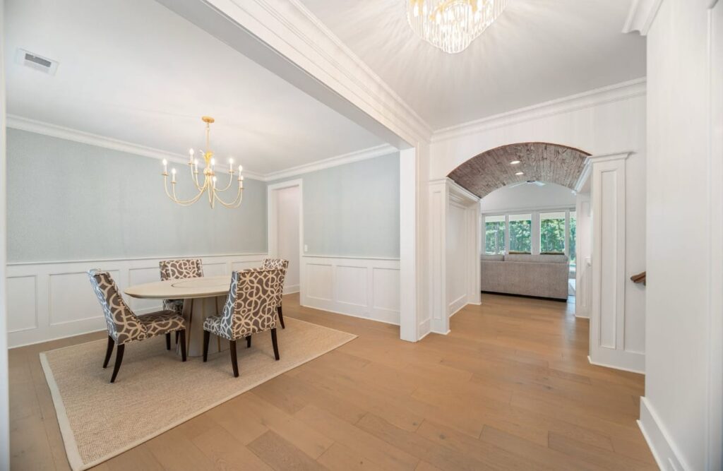 Elegant dining room with light blue walls, white wainscoting, round table, patterned chairs, and arched doorway leading to sunroom.