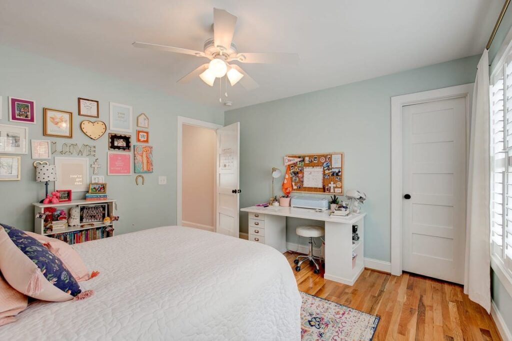 A bright, organized bedroom with mint green walls, white ceiling fan, wooden floors, desk area, and colorful wall art and decorations.