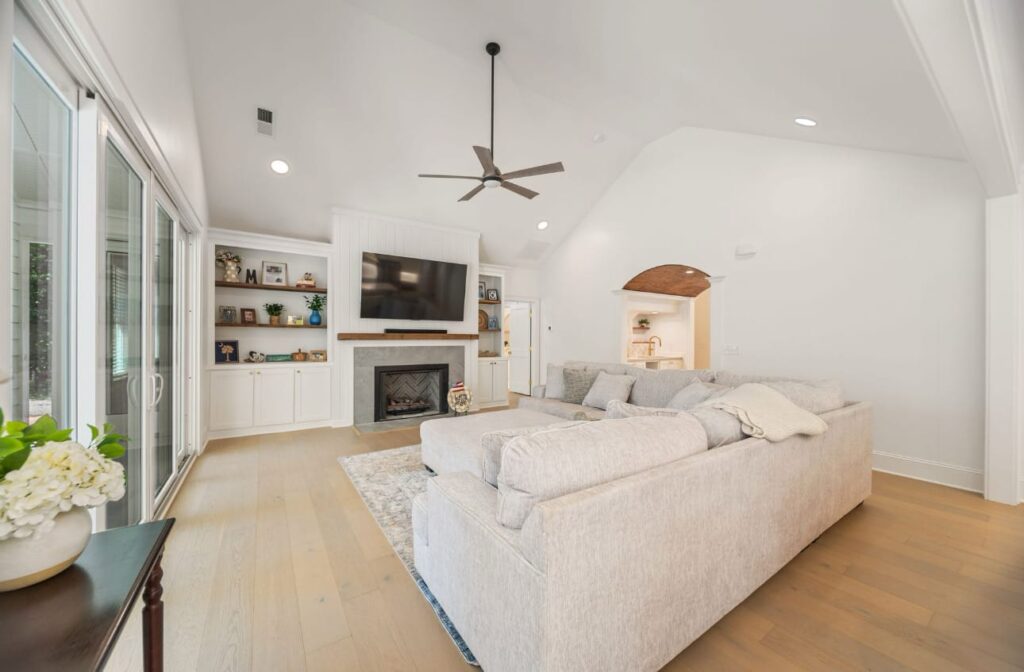 Spacious modern bedroom with vaulted ceiling, fireplace, built-in shelving, and hardwood floors.