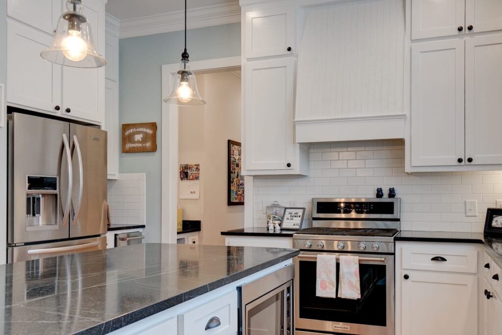 Modern kitchen with white cabinetry, stainless steel appliances, gray countertops, white subway tile backsplash, and pendant lighting.