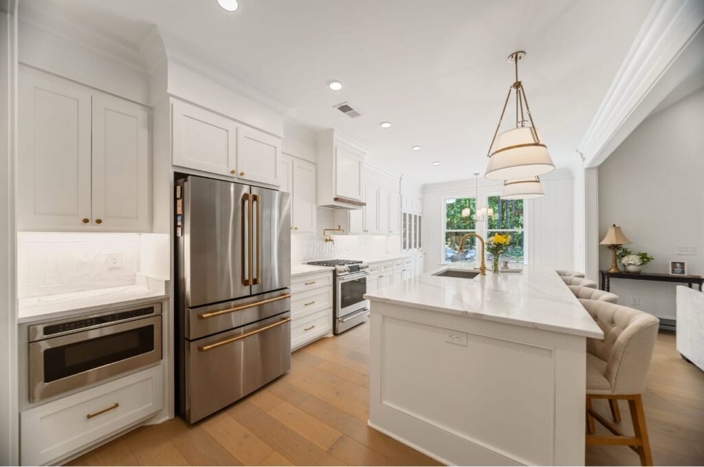 Modern white kitchen with stainless steel appliances, island countertop, and pendant lighting over sink.