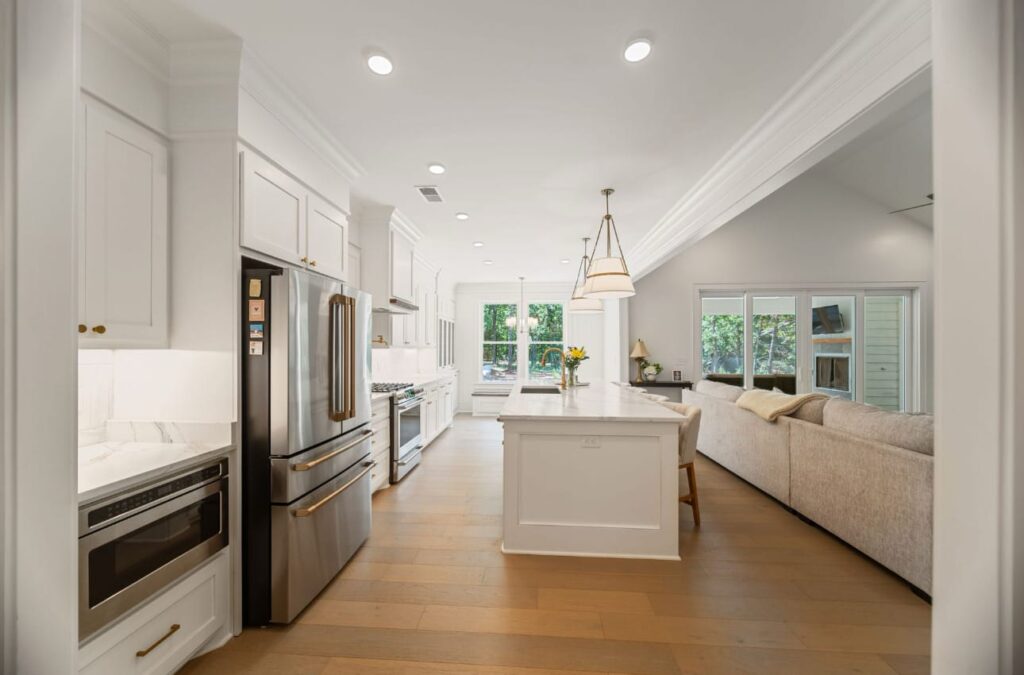 Modern open-concept kitchen and living room with white cabinetry, stainless steel appliances, island, and hardwood floors.