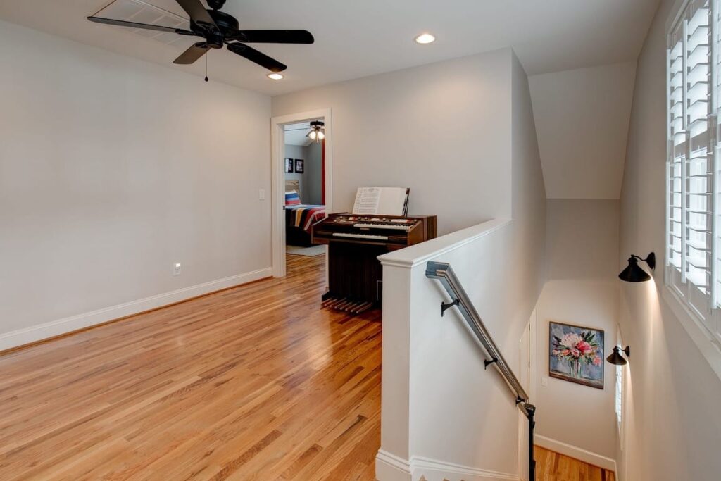 Spacious loft room with hardwood floors, ceiling fan, staircase railing, and foosball table in background.