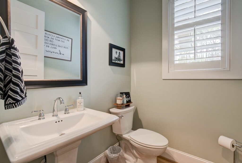 Modern bathroom with pedestal sink, toilet, and window with shutters