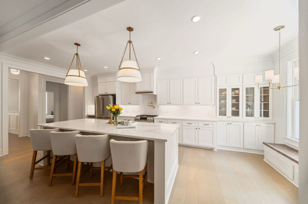 Modern white kitchen with island seating, pendant lights, and stainless steel appliances.