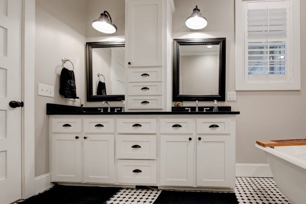 Modern bathroom with dual vanity, black countertop, white cabinetry, framed mirrors, pendant lighting, and black and white tile flooring.