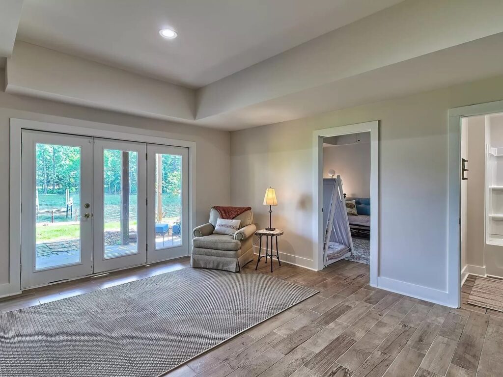 Modern home interior with glass doors, armchair, lamp, and hardwood flooring overlooking outdoor patio area.