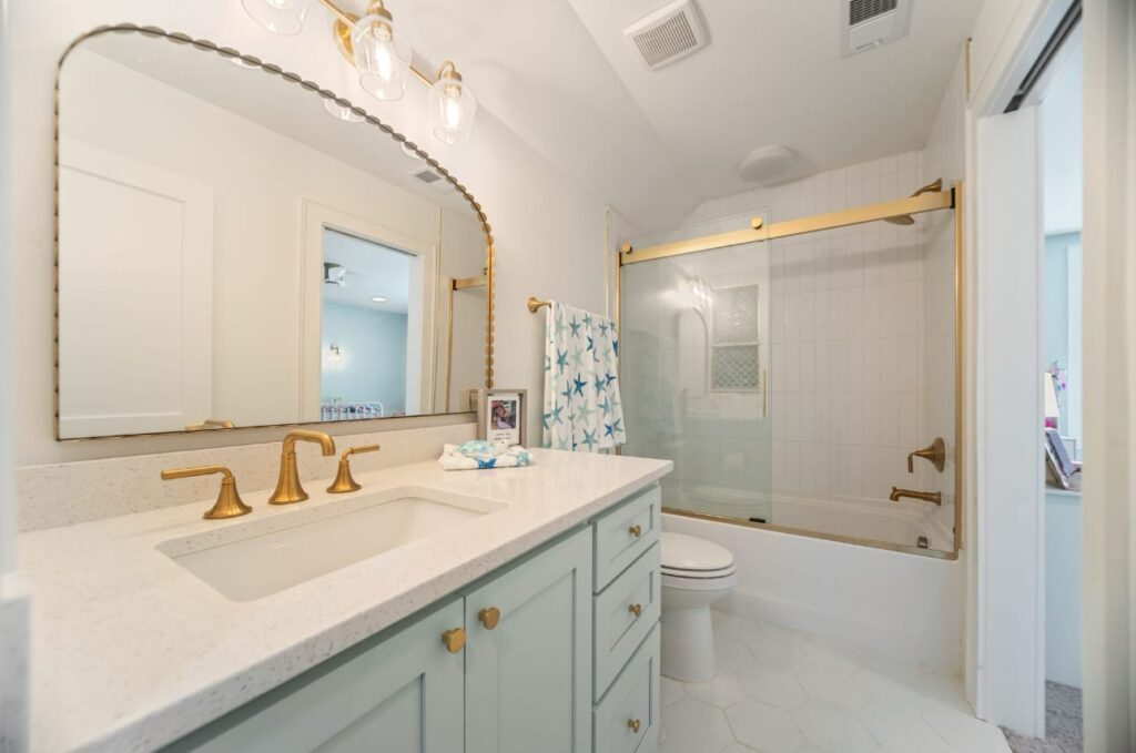 Modern bathroom with light green vanity, white marble countertop, gold fixtures, and glass shower enclosure