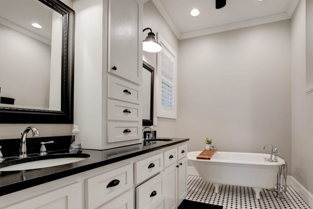 Modern bathroom with white cabinetry, black countertops, dual vanity, freestanding tub, and black and white checkered floor.