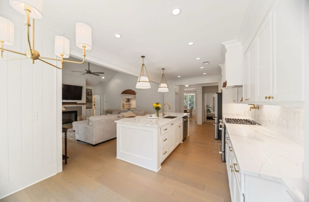 Modern open-concept kitchen and living room with white cabinetry, marble countertops, brass fixtures, and hardwood flooring.
