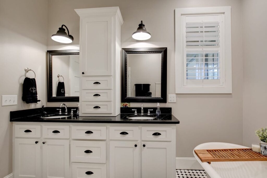 Modern bathroom with dual vanity, white cabinetry, black countertops, framed mirrors, and pendant lighting.