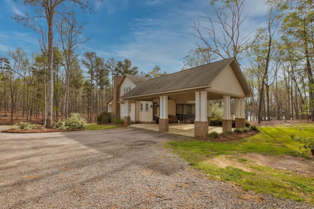 Modern farmhouse with brick columns and covered porch set on wooded property with gravel driveway