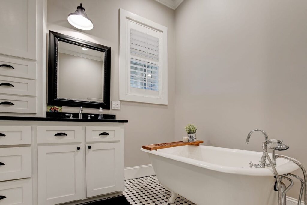 Modern bathroom with white vanity, black-framed mirror, freestanding white bathtub, and black-and-white checkered floor.