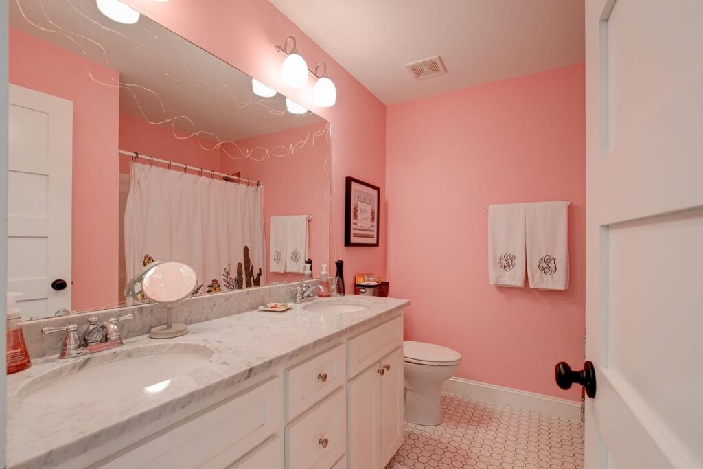 Pink bathroom with white vanity, marble countertop, large mirror, and matching tile flooring.